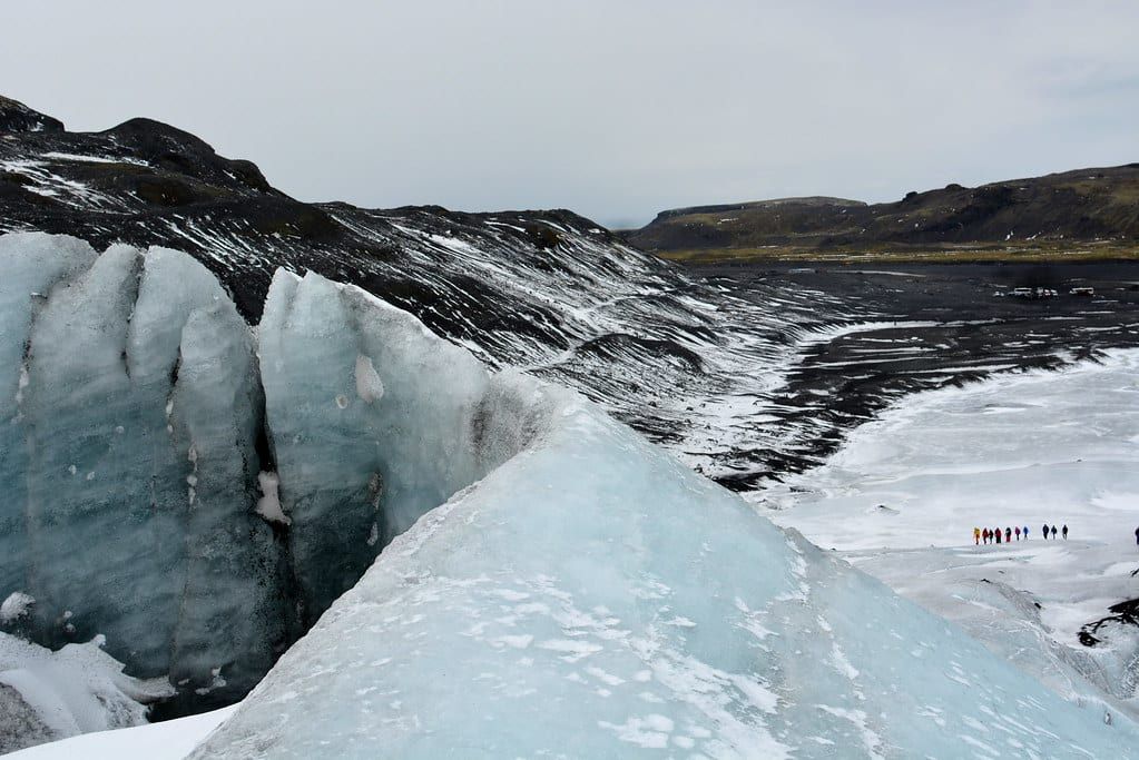 Una gran cresta de hielo azul y una grieta profunda en el glaciar Sólheimajökull con vistas al terreno volcánico oscuro.