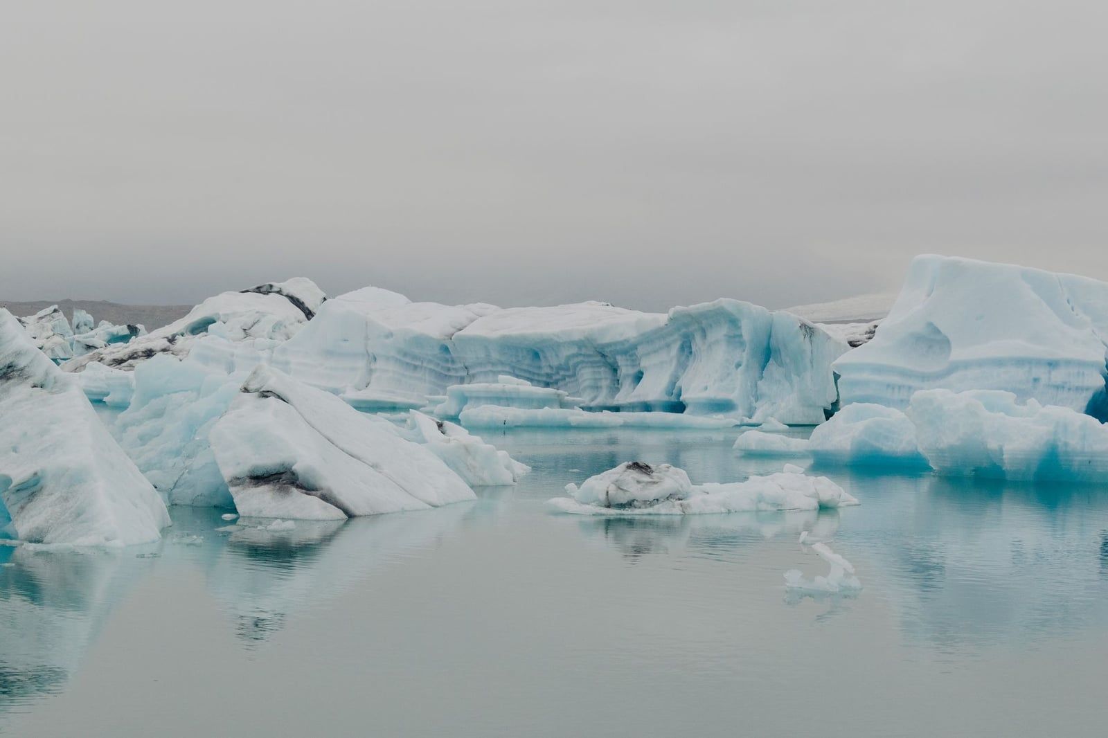 Small icebergs drift across the calm waters of a glacier lagoon at Sólheimajökull Glacier in Iceland.